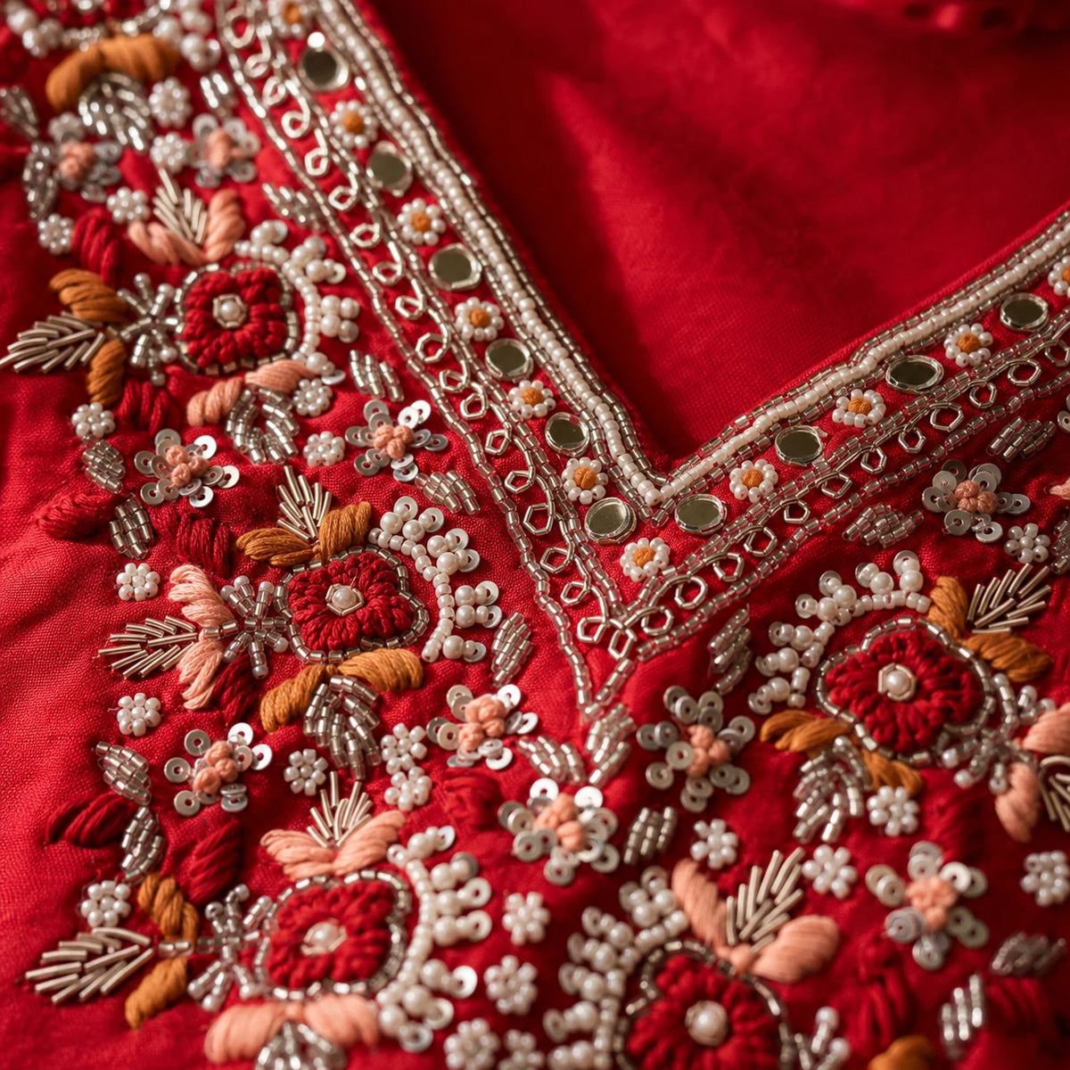 Close-up of a red embroidered blouse neckline with intricate floral embroidery, sequins, and metallic mirror work.