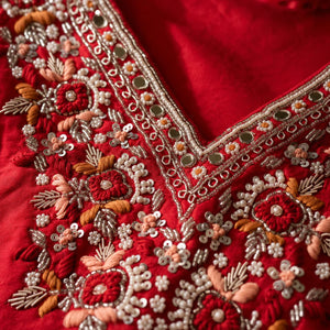 Close-up of a red embroidered blouse neckline with intricate floral embroidery, sequins, and metallic mirror work.