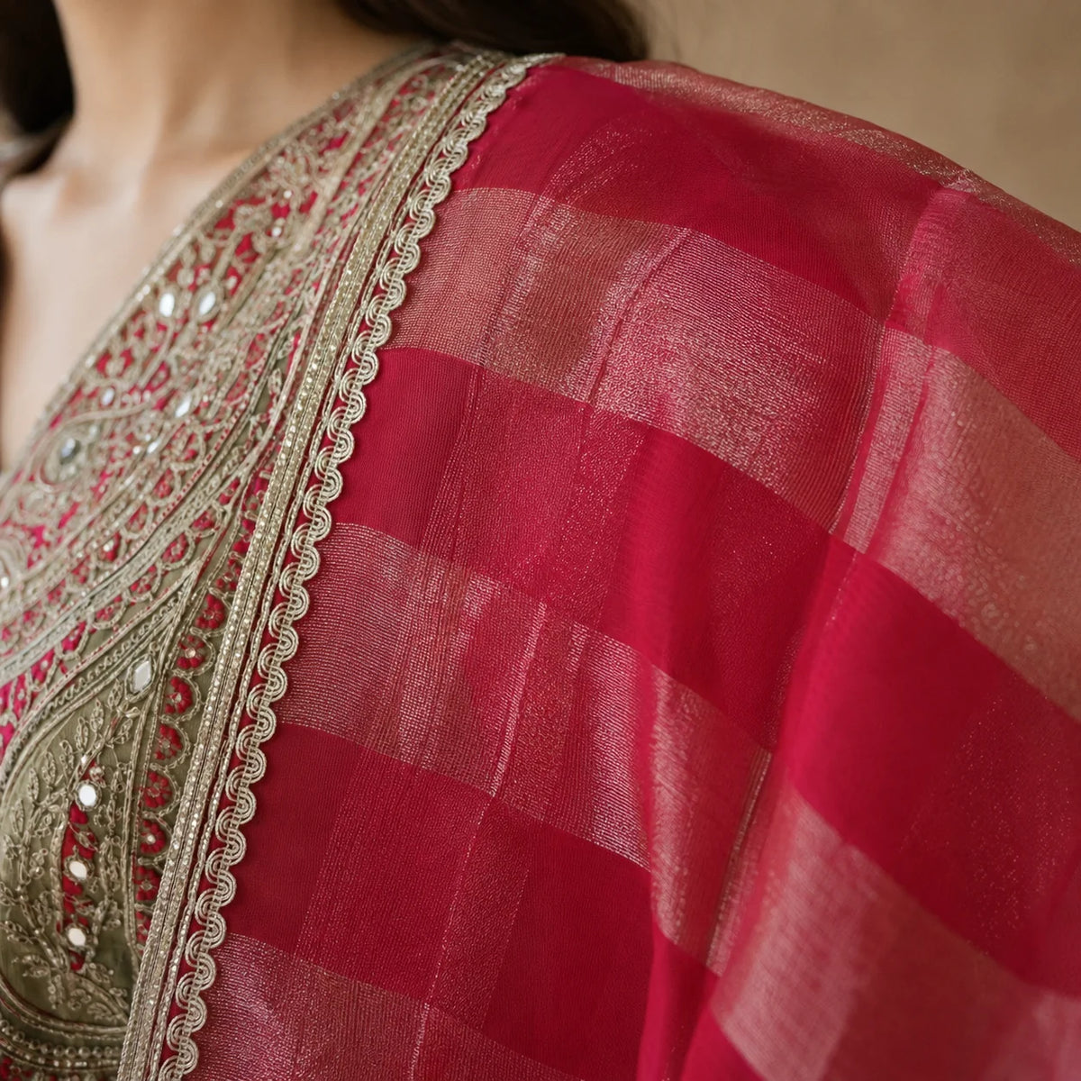 A close-up of a red and pink checkered saree with a gold embroidered border and mirror work, worn by a model.