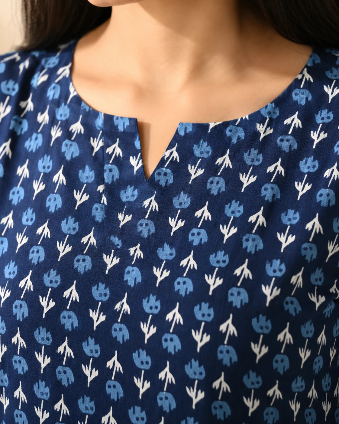Close-up of a person wearing a navy blue top with a repeating light blue and white floral block print pattern and a split neckline.