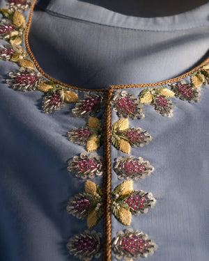 Close-up of a blue-gray embroidered garment neckline with metallic gold thread, pink beaded floral motifs, and green leaf details.