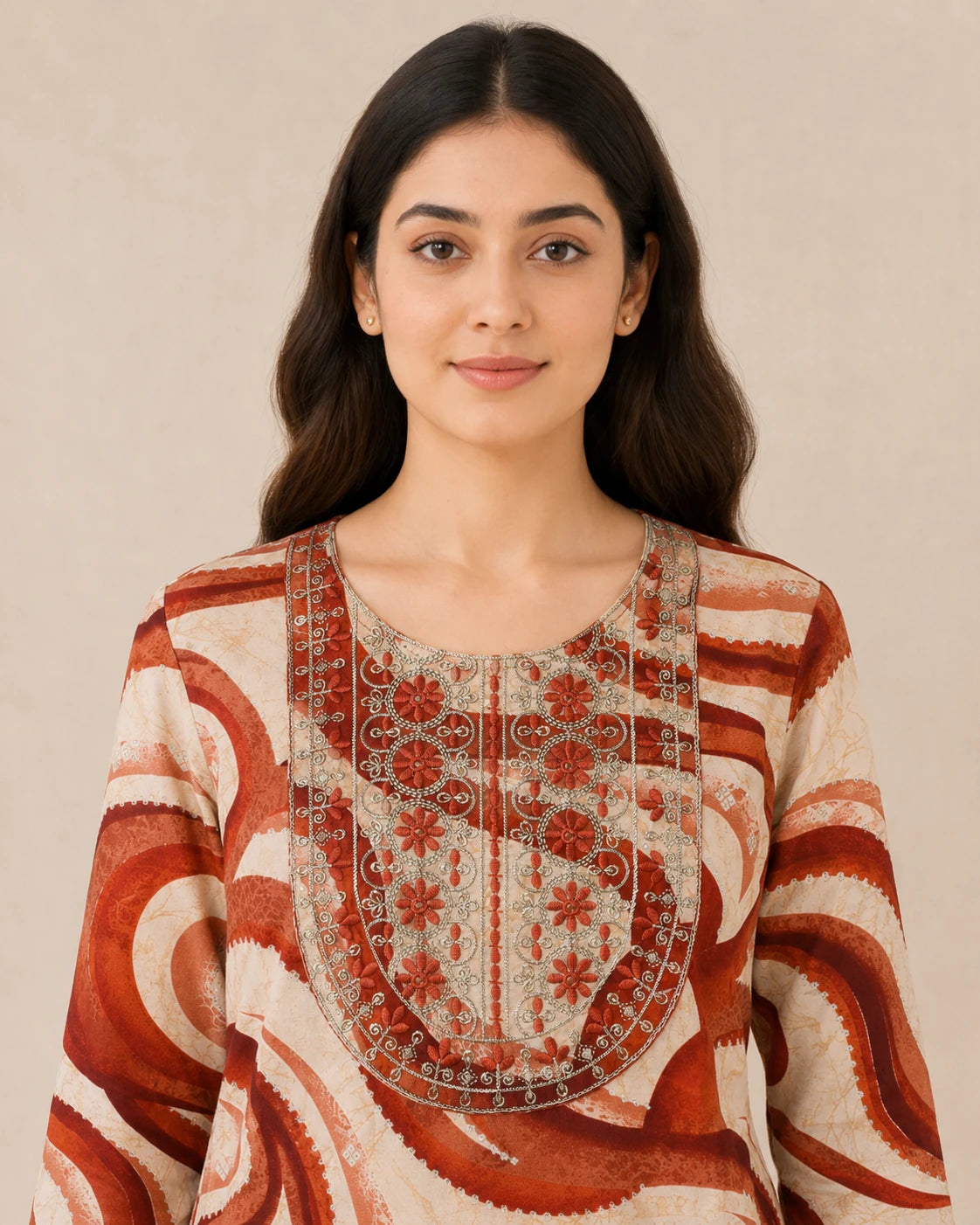 A woman wearing a cream-colored tunic top with rust-red and brown abstract swirl patterns and a detailed embroidered yoke, set against a plain beige background.