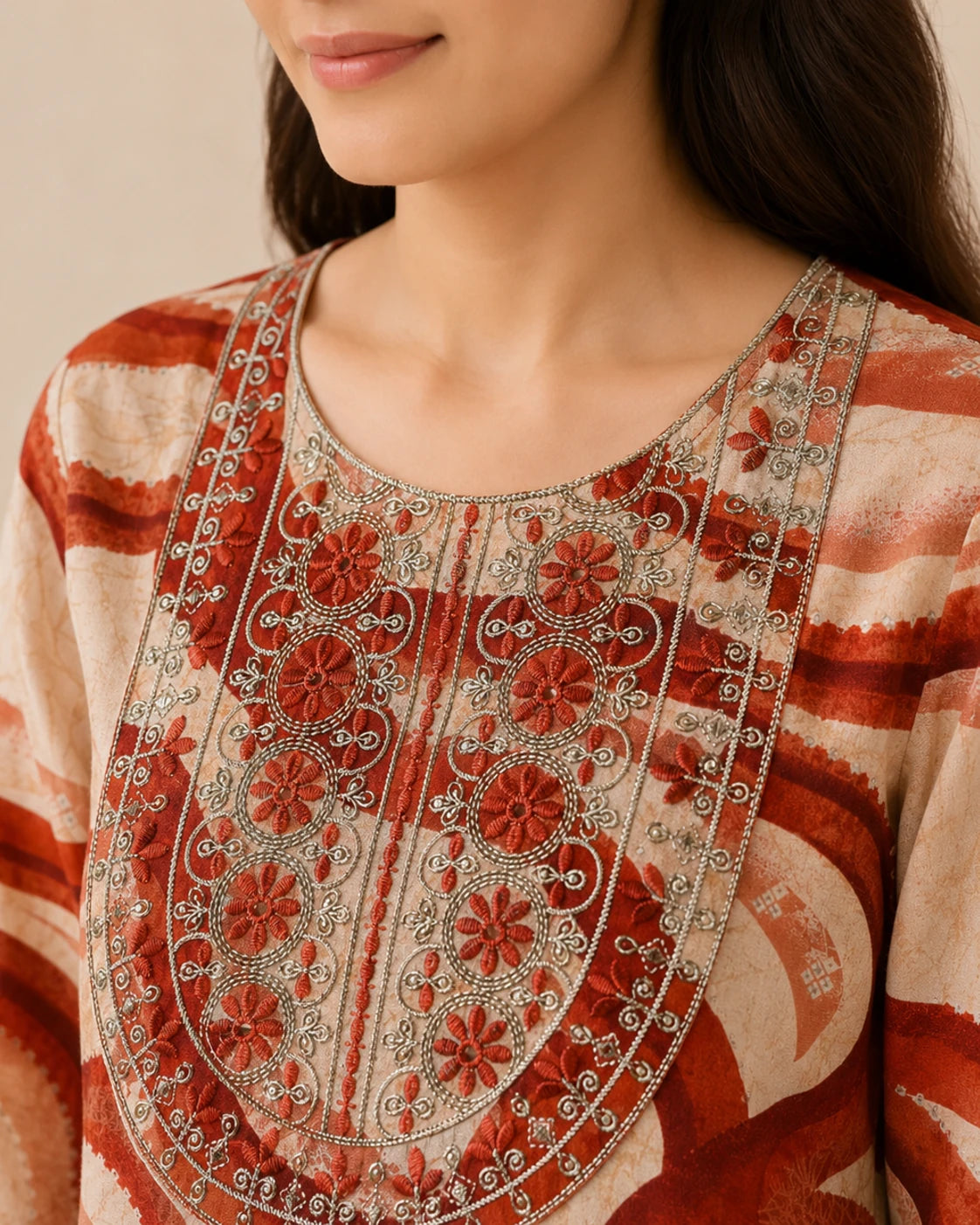 Close-up of a woman wearing a beige and rust-red printed kurta with detailed floral embroidery and silver mirror work around the neckline.