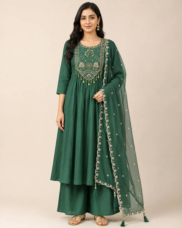 A woman modeling a dark green traditional Indian salwar kameez set with an embroidered yoke and a matching sheer dupatta, set against a plain beige studio background.