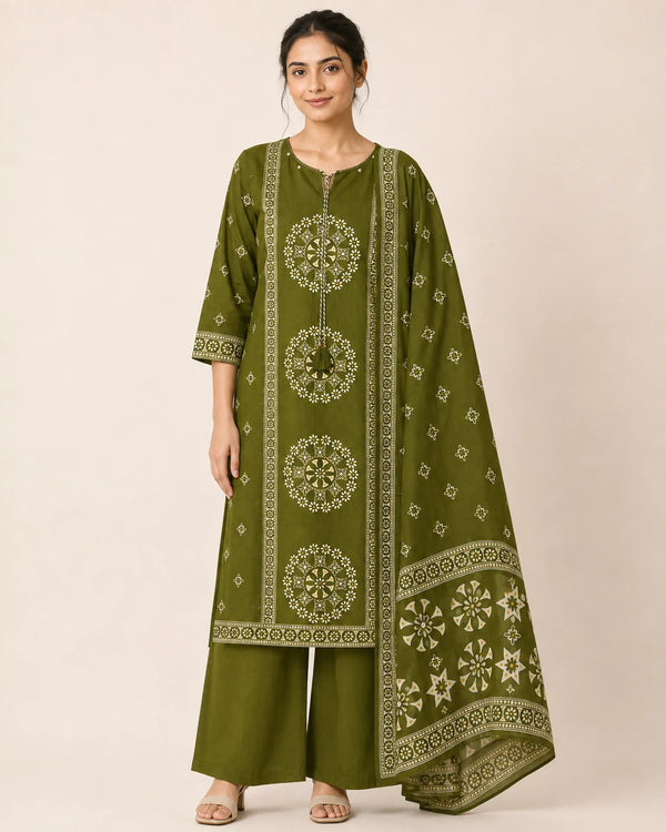A woman modeling an olive green three-piece traditional outfit with beige geometric and mandala embroidery, consisting of a long kurta, wide-leg pants, and a matching dupatta, set against a plain beige studio background.
