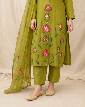 An olive green salwar kameez suit set with pink and brown floral embroidery, paired with matching olive green pants and a sheer olive green dupatta, shown on a model against a neutral beige backdrop.