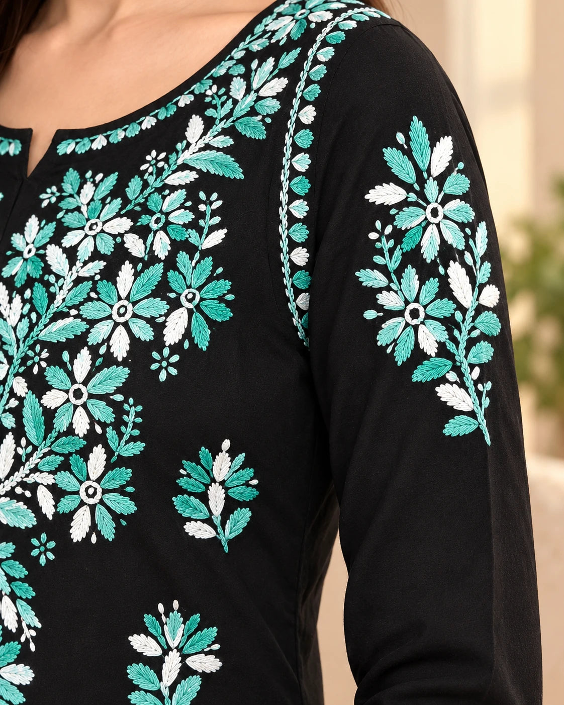 Close-up of a black long-sleeve top with intricate floral embroidery in teal and white on the chest and sleeve.