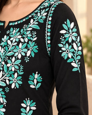 Close-up of a black long-sleeve top with intricate floral embroidery in teal and white on the chest and sleeve.