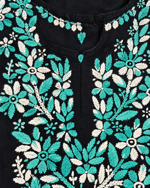 Close-up of a black garment featuring intricate floral embroidery in turquoise and off-white, with a small central button closure at the neckline.