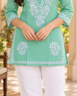 Close-up of mint green chikankari kurti hem with white floral buttis and a leaf-pattern embroidered border along the hem and slits