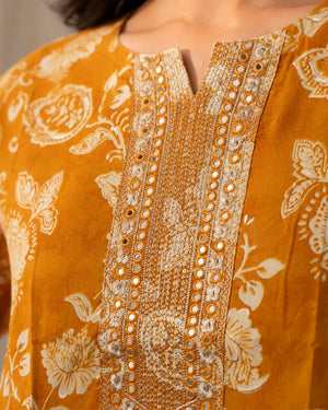 Close-up of a mustard yellow embroidered tunic with white floral print and ornate metallic mirror-work detailing on the front placket.