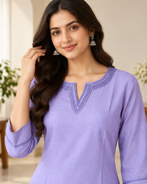 A woman wearing a lavender purple kurta with a split V-neckline and embroidered detailing, posed in a softly lit indoor setting.