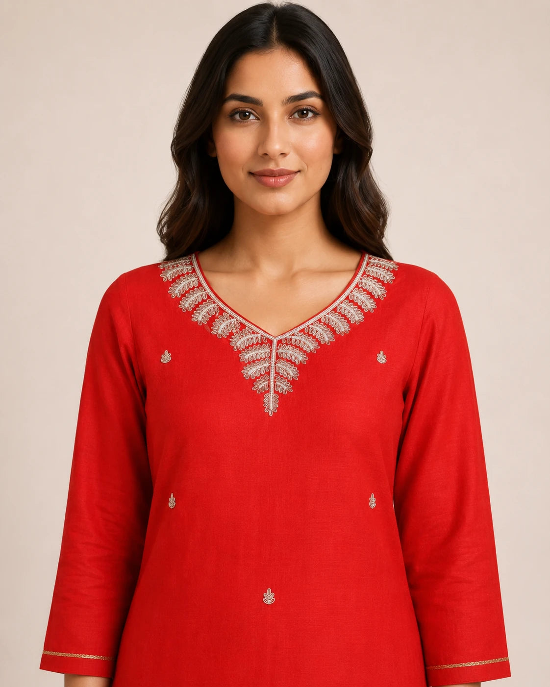 A woman wearing a bright red long-sleeve kurta with intricate silver and white embroidery around the V-neckline and small matching embroidered motifs on the chest and hem, set against a plain beige background.