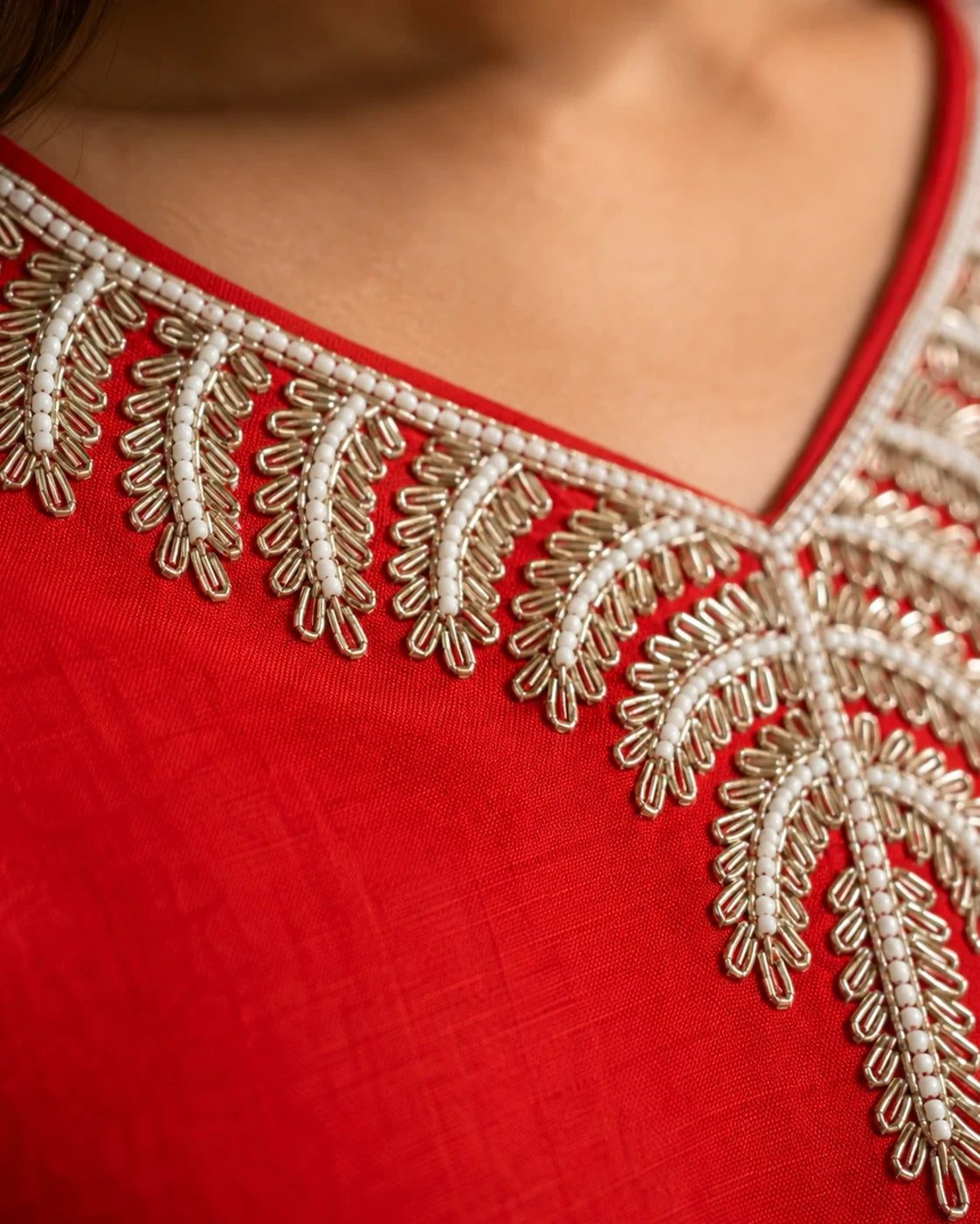 Close-up of a red fabric garment with ornate beige and white embroidered neckline detailing.