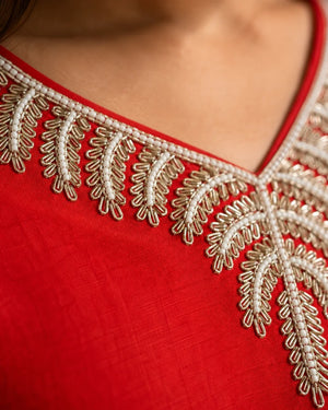 Close-up of a red fabric garment with ornate beige and white embroidered neckline detailing.