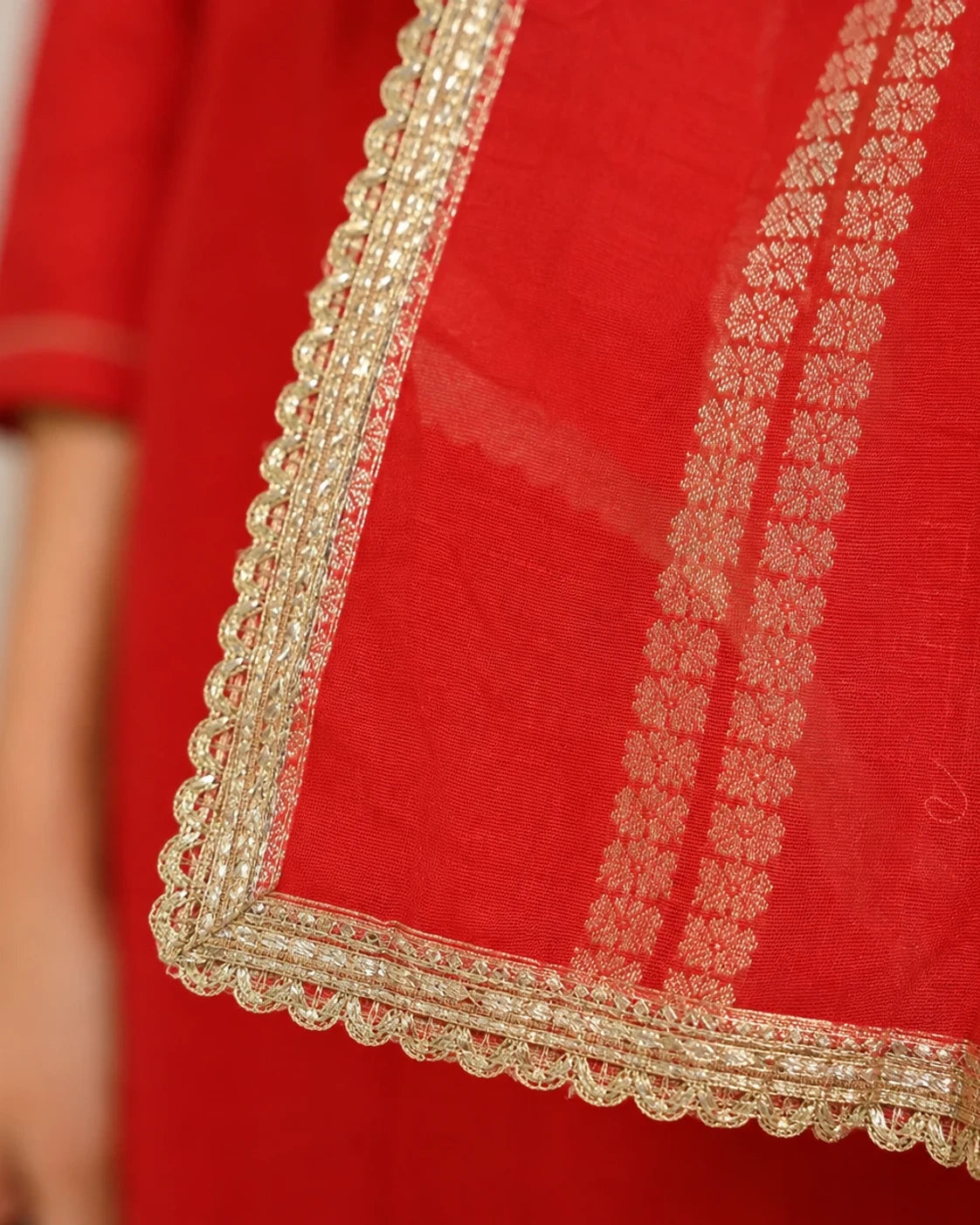 Close-up of a red fabric garment with ornate gold embroidered borders and matching gold floral patterned detailing.