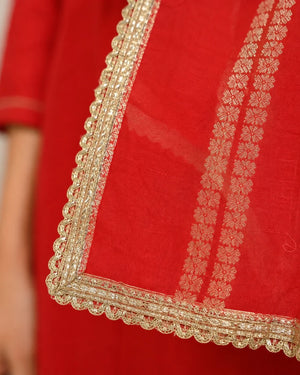 Close-up of a red fabric garment with ornate gold embroidered borders and matching gold floral patterned detailing.