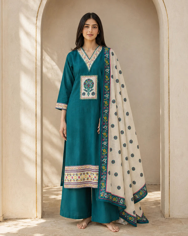 A woman wearing a teal kurta set with multicolor embroidery and a cream dupatta with blue floral motifs and a patterned border.